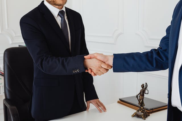 two people shaking hands across a desk with a statue of lady justice between them