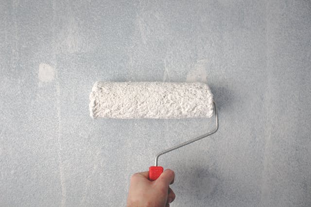 a white paint roller applying primer to a wall