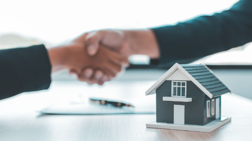 People shaking hands over a lease agreement document next to a mini house model.